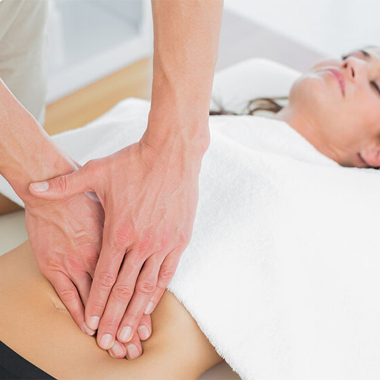 A women is partially covered by white towel during a therapeutic massage.