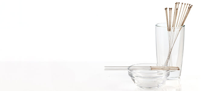 Acupuncture needles being displayed in a glass and on a glass bowl