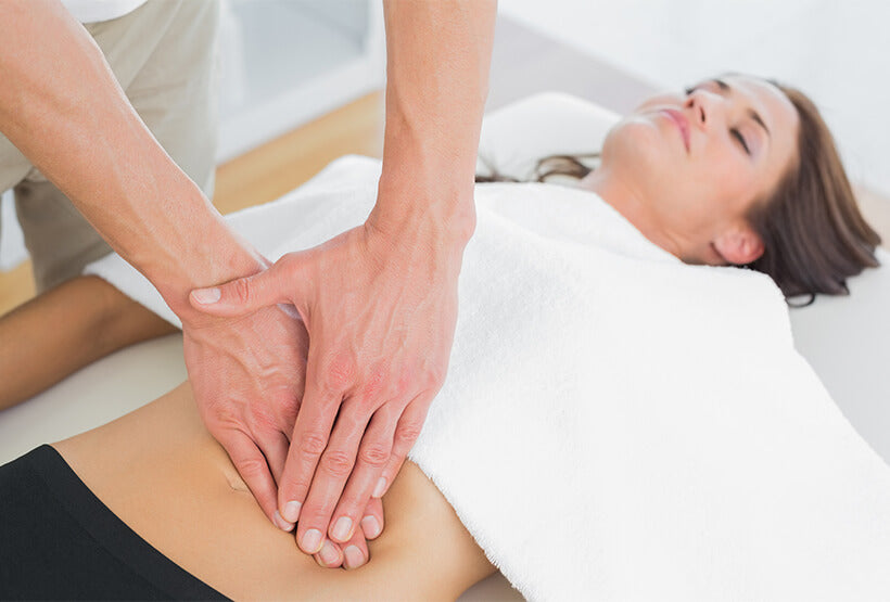 A women is partially covered by white towel during a therapeutic massage.