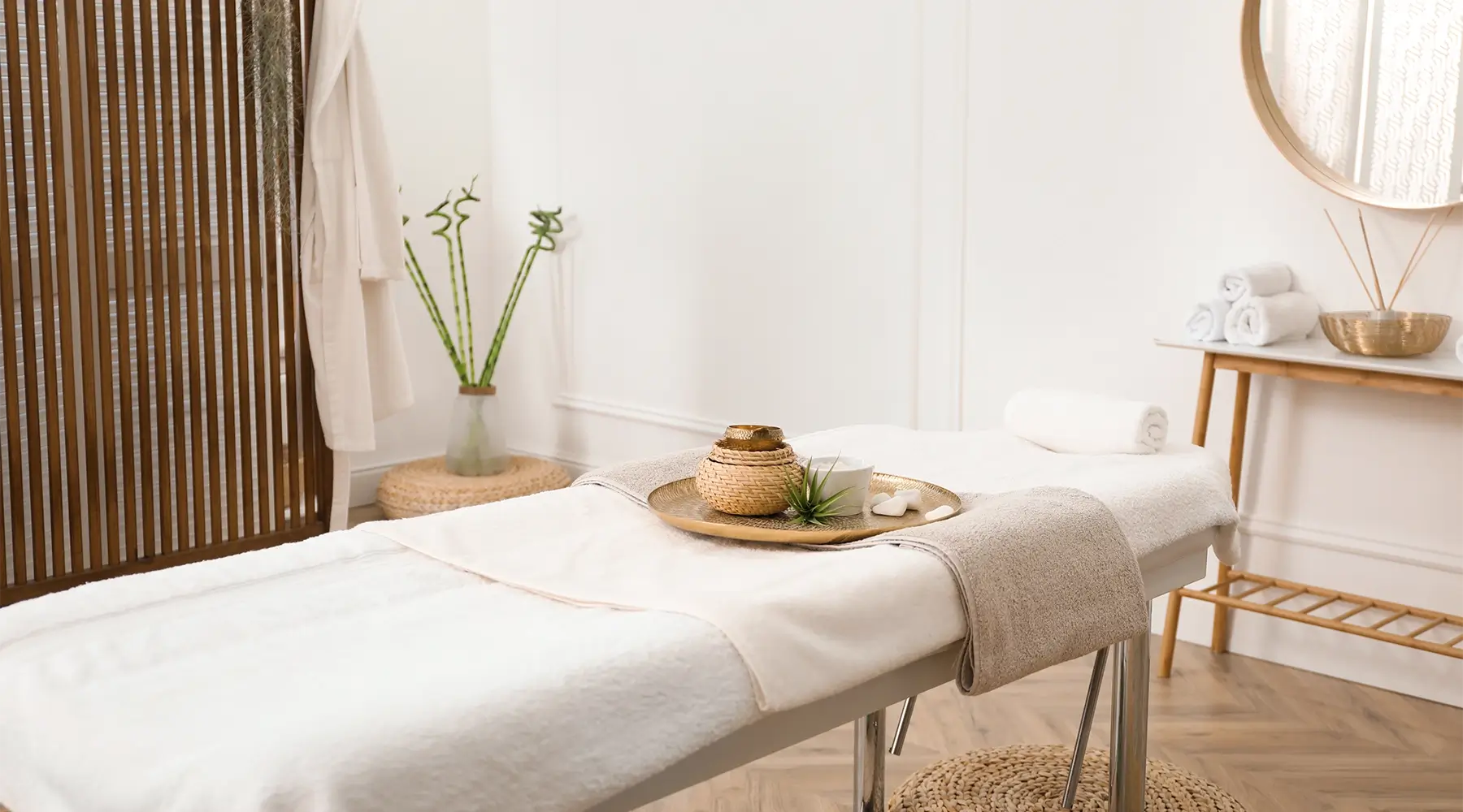 Bright professional massage treatment room with a padded table, fresh white linens, blanket, towels and comfort accessories