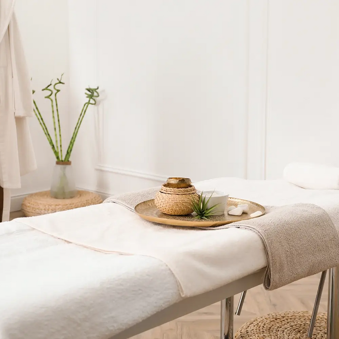 Bright professional massage treatment room with a padded table, fresh white linens, blanket, towels and comfort accessories