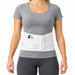 A woman wearing a white CorFit lumbosacral spinal support belt over a gray t-shirt and dark gray leggings, shown from the neck down against a plain white background.