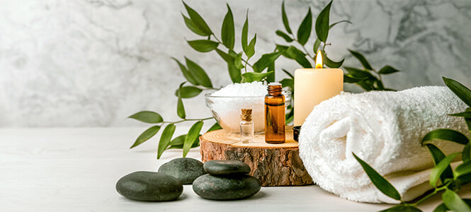 Hot stones a towel  salts and essential oil bottles with a candle sitting on a piece of wood