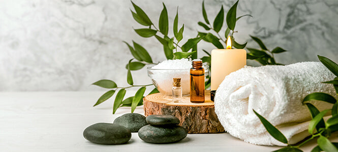 Hot stones a towel salts and essential oil bottles with a candle sitting on a piece of wood