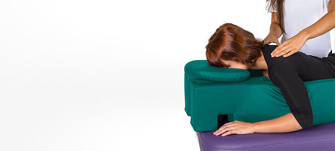 Women lying in a body support system on top of a portable treatment table being massaged