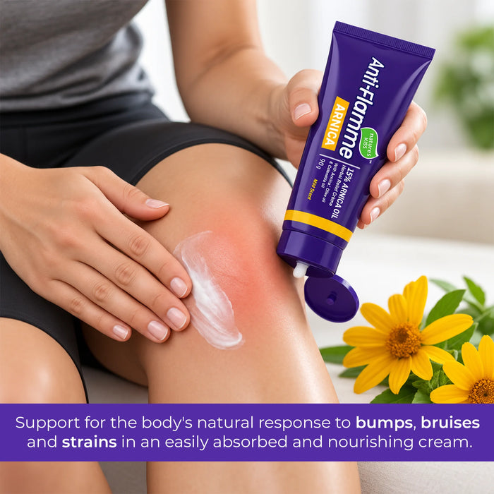 A person applies white cream to a red, bumped knee while holding a purple tube of Anti-Flamme Arnica  Pain Relief cream 90g. Yellow arnica flowers are visible in the foreground, and a purple text banner is at the bottom.