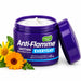 A purple jar of Nature's Kiss Anti-Flamme Soothing Everyday Herbal Relief Crème 45g with its lid leaning against it, shown on a white background with yellow flowers and green leaves as props.