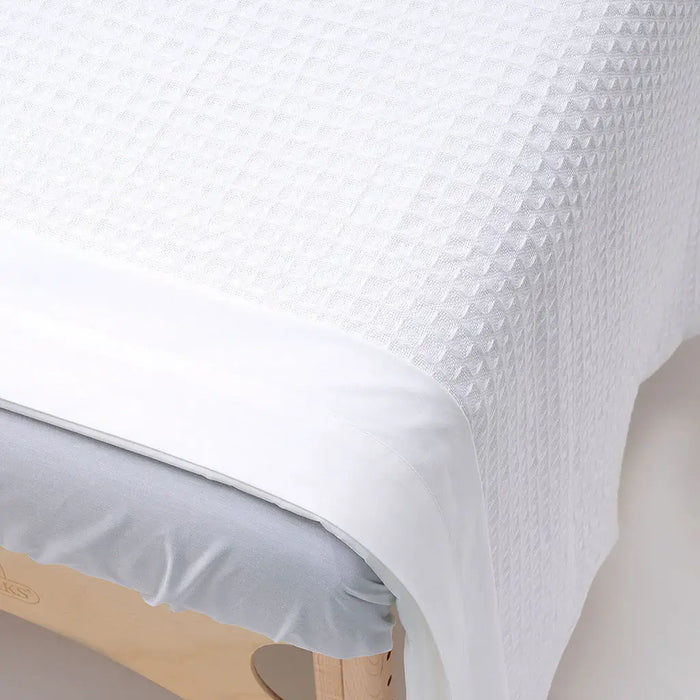 Close-up of a textured white waffle weave massage table blanket on a bed with a wooden headboard.