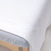 Close-up of a textured white waffle weave massage table blanket on a bed with a wooden headboard.