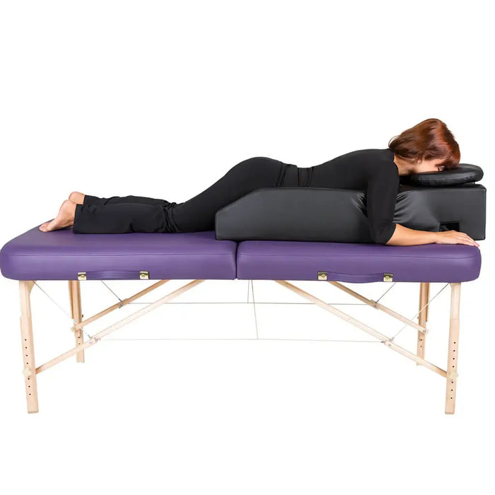 Person lying on a purple massage table with black cushions on a white background