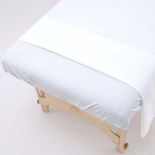 White bed sheet on a wooden massage table against a white background