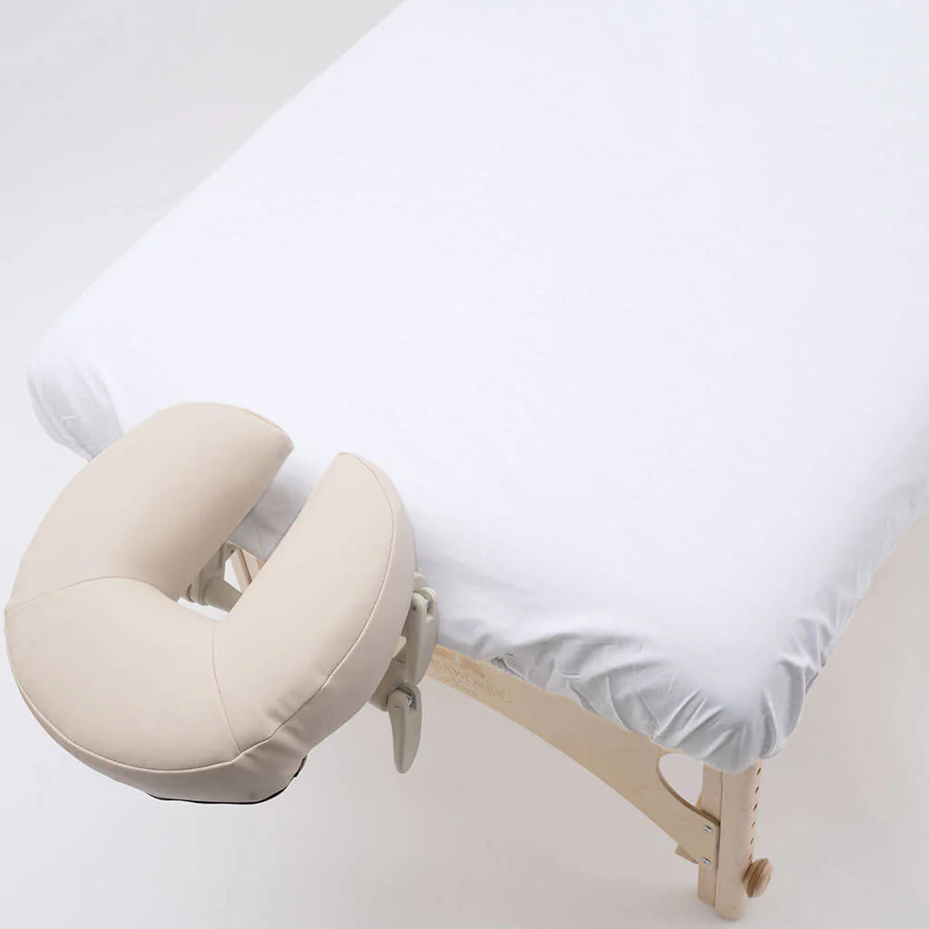 Beige U-shaped pillow on a massage table with white sheets