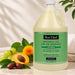A gallon of Bon Vital Massage Gel stands on a light stone surface with decorative fruit and leaves around it. The bottle is filled with a pale yellow gel and has a green front label reading Bon Vital Massage Gel.