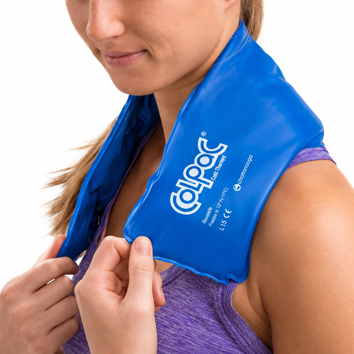 A woman wearing a blue Chattanooga Colpac cooling neck wrap around her neck, with her hands adjusting the wrap. She is wearing a purple athletic tank top against a clean white background.