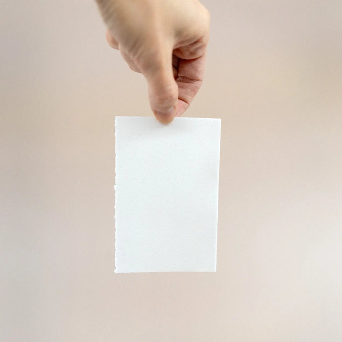 Hand holding an Eco-Max Laundry Detergent Strip against a beige background